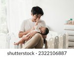 Small photo of Happy young Asian father feeding cute baby boy with milk from baby bottle. Little baby drinking milk and touching on face father. Fathers day concept.
