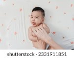 Cute Asian little boy in good mood sticks tongue out while Mother’s Finger Applying Skin Care Lotion on Her Son’s Arm in Closeup Shot, Embracing the Concept of Baby Care.