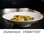 Buckwheat dumplings with fresh mushrooms served on a white plate over black background.