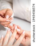 Small photo of French manicure. Manicure master drawing white varnish on the nail tip with a thin brush, close up