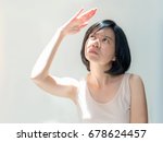 Portrait of a beautiful Asian girl with short black hair covering face by hand of bright sun light. Middle aged woman in a beige dress protecting her face from solar light. Skin care or beauty concept