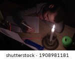 Tired schoolboy with candle in complete darkness doing homework. Power outage, blackout, concept image. 