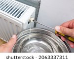 Small photo of Bleed valve in heating radiator. Hand draining air for adjusts heating system at home. Preparing the house for the new cold autumn or winter season.