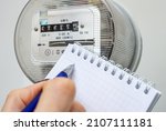 Ballpoint pen in hand for writing electricity meter readings. Distribution of electricity in an apartment building, payment of utilities bills, energy savings, symbolic image.