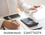 Closeup of person holding bills and calculating them. Notebook, calculator and smartphone lying on desk. Payment concept. Cropped view.