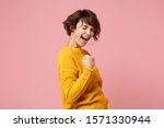 Side view of young brunette woman girl in yellow sweater posing isolated on pastel pink background studio portrait. People sincere emotions lifestyle concept. Mock up copy space. Doing winner gesture