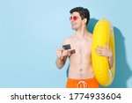 Small photo of Smiling young man guy in eyeglasses isolated on blue background studio portrait. People summer vacation rest lifestyle concept. Mock up copy space. Hold inflatable ring credit bank cank looking aside