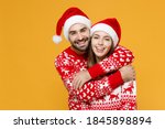 Smiling cheerful young Santa couple friends man woman 20s wearing red sweater Christmas hat hugging isolated on yellow background studio portrait. Happy New Year celebration merry holiday concept