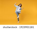 Full length of young overjoyed excited fun student happy woman 20s in denim shirt white t-shirt do winner gesture clench fist celebrating dancing isolated on yellow color background studio portrait.