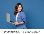 Smiling cheerful beautiful attractive young brunette woman 20s wearing basic jacket standing working on laptop pc computer looking aside isolated on bright blue colour wall background studio portrait