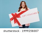 Young redhead chubby overweight woman 30s with curly hair wear casual pink shirt hold big gift certificate coupon voucher card for store isolated on pastel blue background People lifestyle concept.