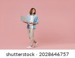 Full length young minded happy man with long curly hair wear blue shirt white t-shirt hold use work on laptop pc computer look aside isolated on pastel plain pink color wall background studio portrait