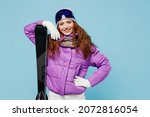 Skier cheerful satisfied happy sporty woman wear warm purple padded windbreaker jacket goggles mask spend extreme weekend in mountains hold ski stand akimbo isolated on plain blue background studio.