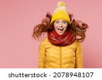 Shocked surprised amazed young woman 20s wears yellow jacket hat mittens keeping mouth wide open jumping have fun enjoy fluttering hair isolated on plain pastel light pink background studio portrait