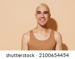 Young smiling minded laughing blond latin american gay man 20s with make up in beige tank shirt looking aside isolated on plain light ocher background studio portrait People lgbt lifestyle concept.