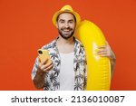 Small photo of Young surprised tourist man in beach shirt hat hold inflatable ring hold in hand use mobile cell phone isolated on plain orange background studio portrait. Summer vacation sea rest sun tan concept.