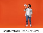 Full size body length promoter young bearded Indian man 20s years old wears blue shirt hold scream in megaphone announces discounts sale Hurry up isolated on plain orange background studio portrait