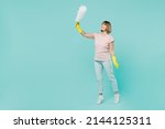 Full body elderly housewife woman 50s in pink t-shirt gloves doing housework hold white duster brush isolated on plain pastel light blue background studio. Housekeeping cleaning tidying up concept.