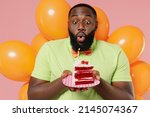 Small photo of Young smiling happy black fun man 20s in green t-shirt bow tie hold bunch of air inflated helium balloons celebrating birthday party sweet cake blow out candle isolated on plain pastel pink background