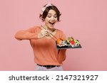 Small photo of Young excited amazed cool fun woman 20s in casual clothes hold in hand eat makizushi sushi roll served on black plate traditional japanese food chopsticks isolated on plain pastel pink background.