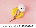 Small photo of Top view full body young woman wearing striped swimsuit cover face with hat lies on inflatable rubber ring in pool isolated on plain pastel pink background. Summer vacation sea rest sun tan concept