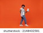 Full size body length side view young bearded Indian man 20s wears blue shirt hold use work on laptop pc computer do winner gesture clenching fists isolated on plain orange background studio portrait