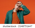 Small photo of Sick ill exhausted sad young brunet man 20s wears red t-shirt green jacket put hands on head having headache suffering from migraine feel bad seedy isolated on plain orange background studio portrait.