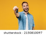 Young smiling happy caucasian man 20s wearing blue shirt white t-shirt hold give car key fob keyless system look camera isolated on plain yellow background studio portrait. People lifestyle concept