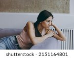Small photo of Side view profile distempered unnerved sad worried frowning minded young latin woman 20s in casual clothes sit on sofa think plan spend time in living room home in own house. People emotions concept