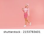 Full body side view young woman 20s with bright dyed rose hair in rosy top shirt hat hold takeaway delivery craft paper brown cup coffee to go walk going isolated on plain light pastel pink background