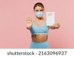 Young athletic fitness trainer instructor woman wear blue tracksuit mask spend time in home gym hold covid-19 certificate show stop gesture isolated on plain pink background. Workout sport concept.