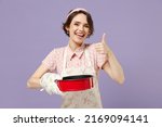 Young housewife housekeeper chef cook baker woman in pink apron holding red non-stick baking form for pie cake show thumb up gesture isolated on pastel violet background Cooking food process concept