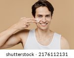 Small photo of Smiling young man he 20s perfect skin in undershirt applying moisturizer, facial cream from container isolated on plain pastel beige background studio. Skin care healthcare cosmetic procedures concept