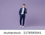 Full size young successful employee business man lawyer 20s wear formal blue suit white t-shirt move stroll hold use mobile cell phone hand in pocket isolated pastel purple background studio portrait