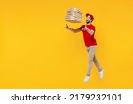 Small photo of Side view full body delivery guy employee man in red cap T-shirt uniform work as dealer courier hold toss up pizza in cardboard flatbox jump high isolated on plain yellow background Service concept.