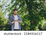 Small photo of Bottom view young smiling man in blue casual shirt walk use mobile cell phone rest relax in spring sunshine forest green city park go down alley outdoors on nature. Urban lifestyle leisure concept.