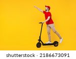 Full body side view delivery guy employee man in red cap T-shirt uniform workwear work as dealer courier ride electric kick scooter isolated on plain yellow background studio portrait. Service concept