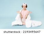 Full length young woman in pajamas jam sleep eye mask rest at home sit wrap covered under blanket duvet do yoga om gesture calm down isolated on pastel blue background Good mood night bedtime concept