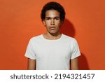 Small photo of Distempered frowning upsed unnerved severe displeased sullen aggrieved young black curly man 20s years old wears white t-shirt looking camera isolated on plain pastel orange background studio portrait