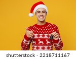 Merry young man wear red knitted christmas sweater Santa hat posing hold car key fob keyless system show thumb up isolated on plain yellow background. Happy New Year 2023 celebration holiday concept