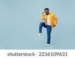 Full body excited young man of African American ethnicity 20s he wear yellow shirt doing winner gesture celebrate clenching fists say yes isolated on plain pastel light blue background studio portrait