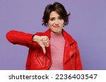 Young displeased disappointed sad woman 20s wearing red leather jacket showing thumb down dislike gesture isolated on plain pastel light purple background studio portrait. People lifestyle concept.