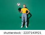 Small photo of Full body young cool happy woman fan wear yellow t-shirt cheer up support football sport team hold in hand toss up soccer ball look camera watch tv live stream isolated on dark green background studio