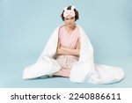 Full length young frowning woman in pajamas jam sleep eye mask rest at home sit wrap covered blanket duvet hold hands crossed folded isolated on pastel blue background Bad mood night bedtime concept