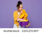 Small photo of Young housekeeper woman wear yellow shirt tidy up hold basin with clean clothes after laundry sniff scent of washing powder isolated on plain pastel light purple background studio. Housework concept