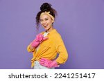 Side view young happy fun woman wear yellow shirt rubber gloves while doing housework tidy up show thumb up wink blink eye isolated on plain pastel light purple background studio. Housekeeping concept