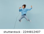 Small photo of Full body young singer happy woman wear knitted sweater jump high sing song in microphone raise up hand isolated on plain pastel light blue cyan background studio portrait. People lifestyle concept