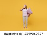 Full body tired young woman she wears purple pyjamas jam sleep eye mask rest relax at home cover mouth with hand yawn hold pillow isolated on plain yellow background studio portrait. Night nap concept