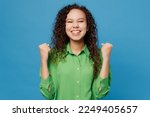 Small photo of Young woman of African American ethnicity 20s she wear green shirt doing winner gesture celebrate clenching fists say yes isolated on plain blue background studio portrait. People lifestyle concept
