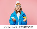 Snowboarder woman wear blue suit goggles mask hat ski jacket use mobile cell phone credit bank card book tour isolated on plain pastel pink background. Winter extreme sport hobby weekend trip concept